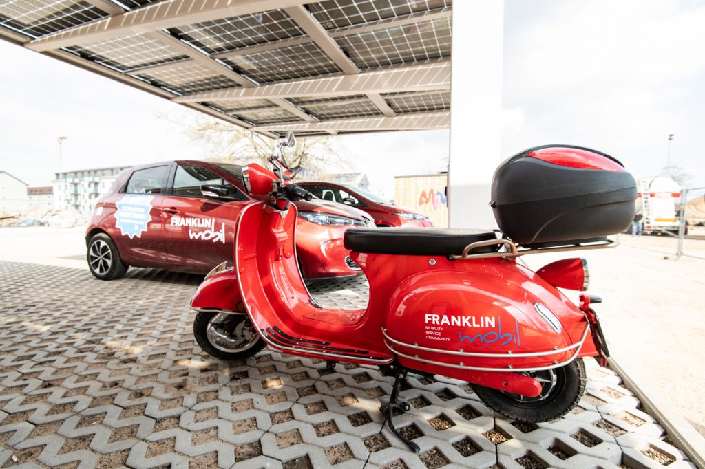 Ein roter Roller im Vordergrund und ein rotes Auto im Hintergrund. Beide Fahrzeuge haben die Aufschrift FRANKLIN Mobil.