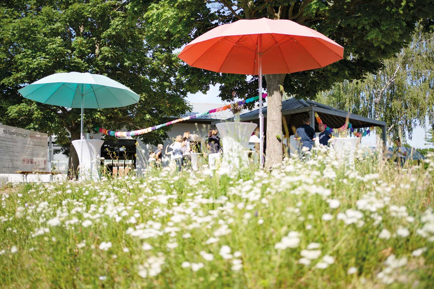 Kleines Fest auf der Wiese vor dem House of Maemories mit Stehtischen und bunten Schirmen.