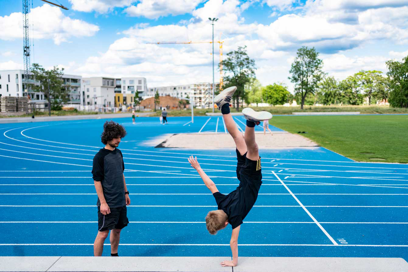 Zwei Jungen stehen an der Franklin Sportanlage. Einer der Jungen macht einen einarmigen Handstand.