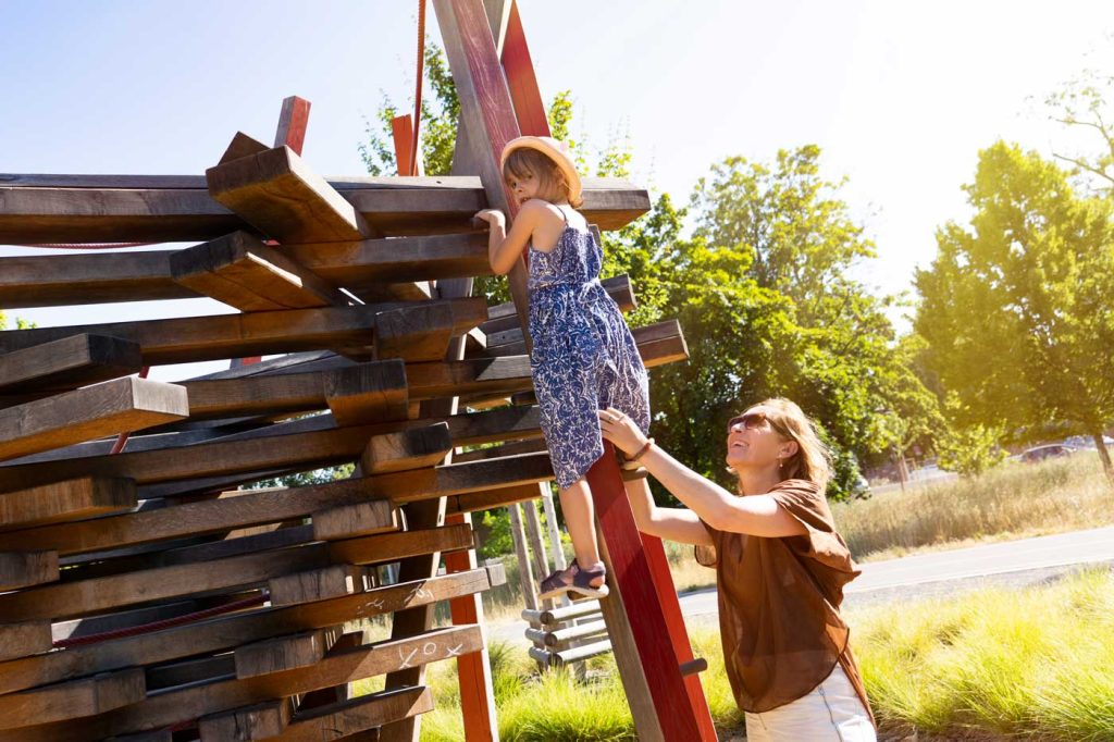 Auf einem Spielplatz hilft eine Mutter ihrer Tochter beim erklettern eines Spielgeräts.