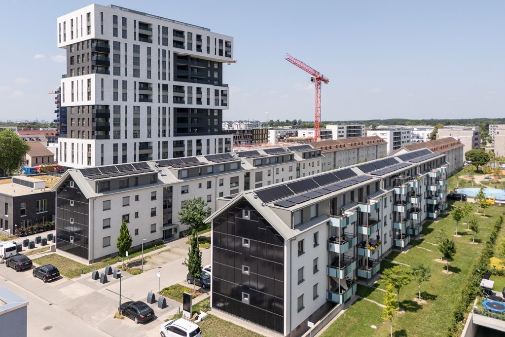 Luftbild von zwei großen Wohnblöcken mit jeweils 4 Stockwerken vor einem Hochhaus in Buchstabenform E.