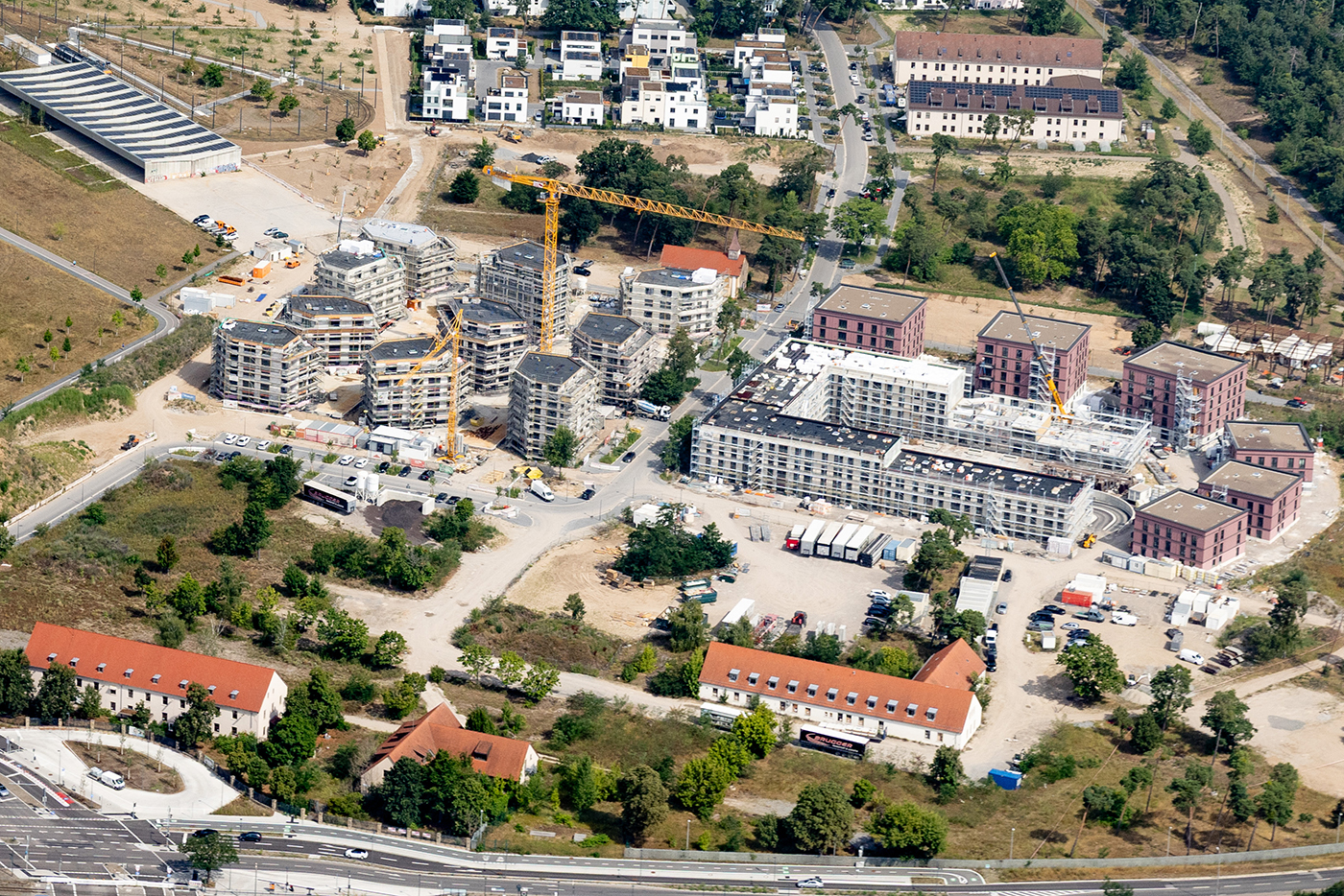 KI-basierte Bildbeschreibung | Luftaufnahme einer Baustelle mit mehreren Gebäuden, die sich in verschiedenen Stadien der Fertigstellung befinden, Kränen, Baugeräten und umliegenden Wohngebieten.