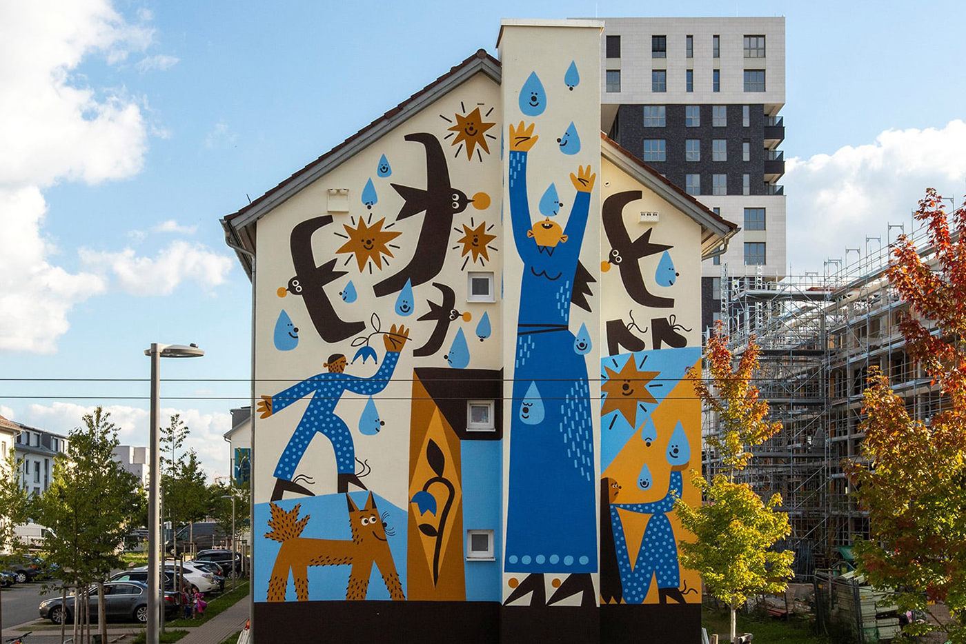 KI-basierte Bildbeschreibung | Eine farbenfrohe Wandmalerei auf einem Gebäude zeigt abstrakte menschliche und tierische Figuren, die nach blauen Wassertropfen greifen, mit einer modernen Stadtlandschaft im Hintergrund.