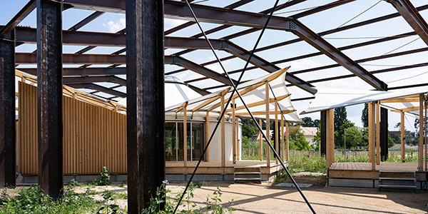 KI-basierte Bildbeschreibung | Stahlgerüst über einem Jurten-Holzgebäude mit einigen Stoffverkleidungen, umgeben von Vegetation und offener Landschaft.