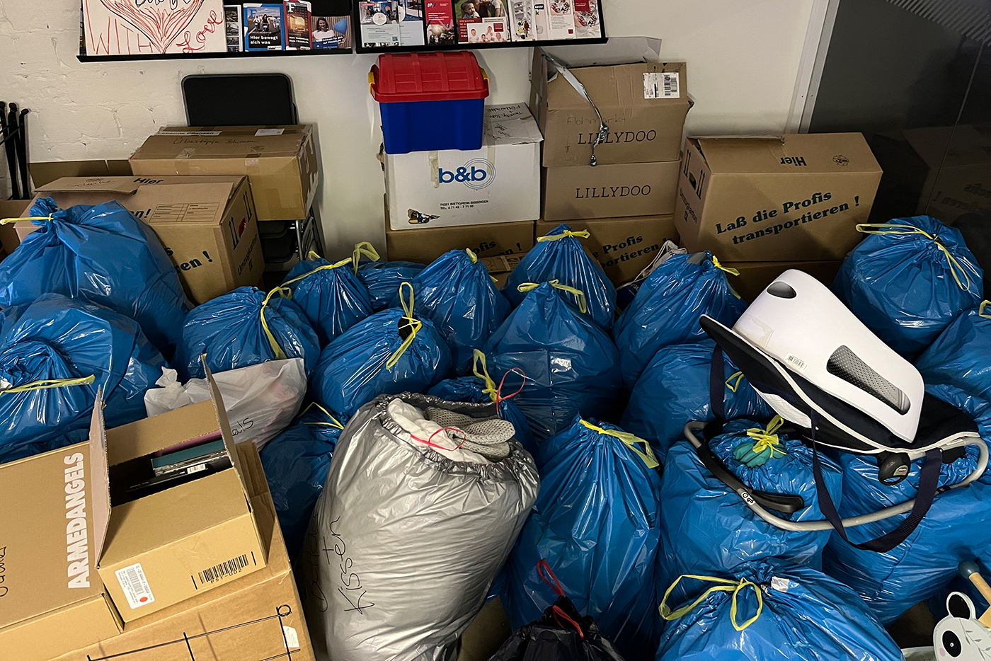 KI-basierte Bildbeschreibung | Ein Raum voller gepackter Kartons, blauer Plastiktüten, die mit gelben Schnüren verschnürt sind, und einiger anderer Dinge, darunter ein Staubsauger.