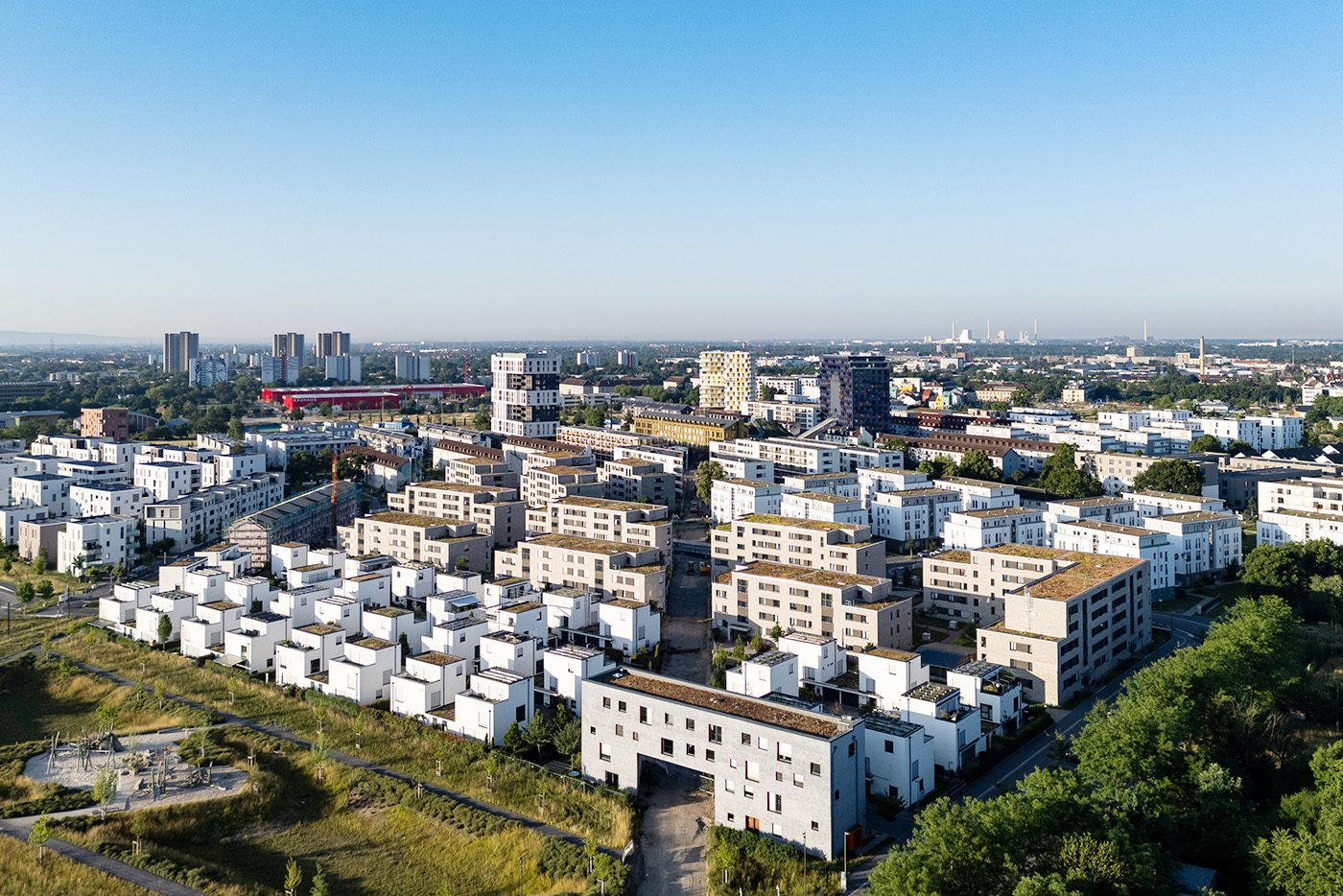 KI-basierte Bildbeschreibung | Luftaufnahme eines modernen Wohnviertels mit weißen und beigen Wohnblocks, darunter der stilvolle Franklin-Komplex, umgeben von Grünflächen und mit der Stadtkulisse im Hintergrund unter einem strahlend blauen Himmel.