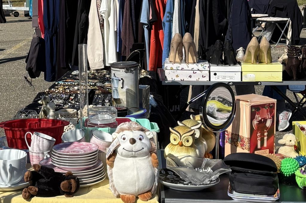 KI-basierte Bildbeschreibung | Auf einem Flohmarktstand liegen Stofftiere, Geschirr, Schuhe, Schmuck und verschiedene Haushaltsgegenstände aus.