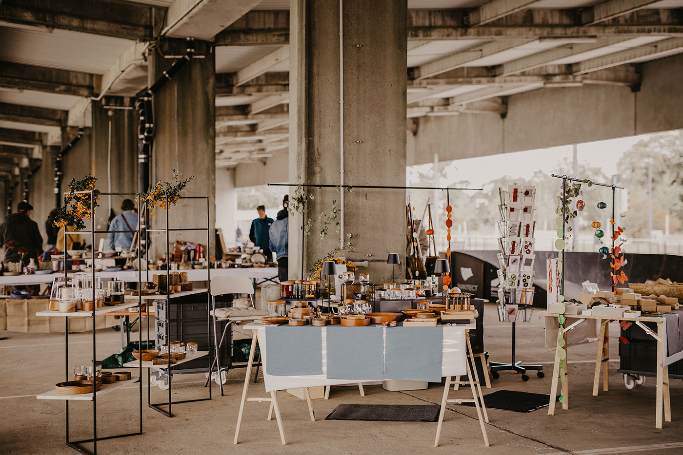 KI-basierte Bildbeschreibung | An Marktständen unter einem Betonbau werden verschiedene handgefertigte Waren, Töpferwaren und Dekorationsartikel angeboten, während im Hintergrund einige Leute stöbern.